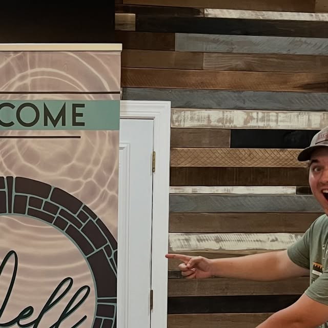 A young man pointing to The Well welcome sign