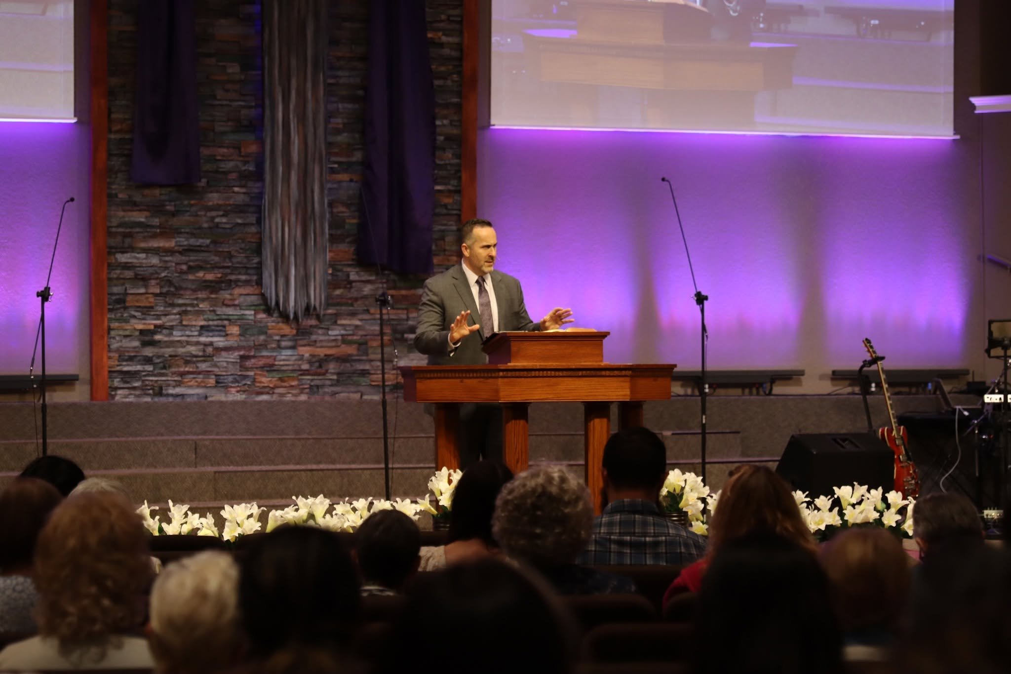 Pastor speaking at the pulpit in a sanctuary with purple stage lighting and a seated congregation