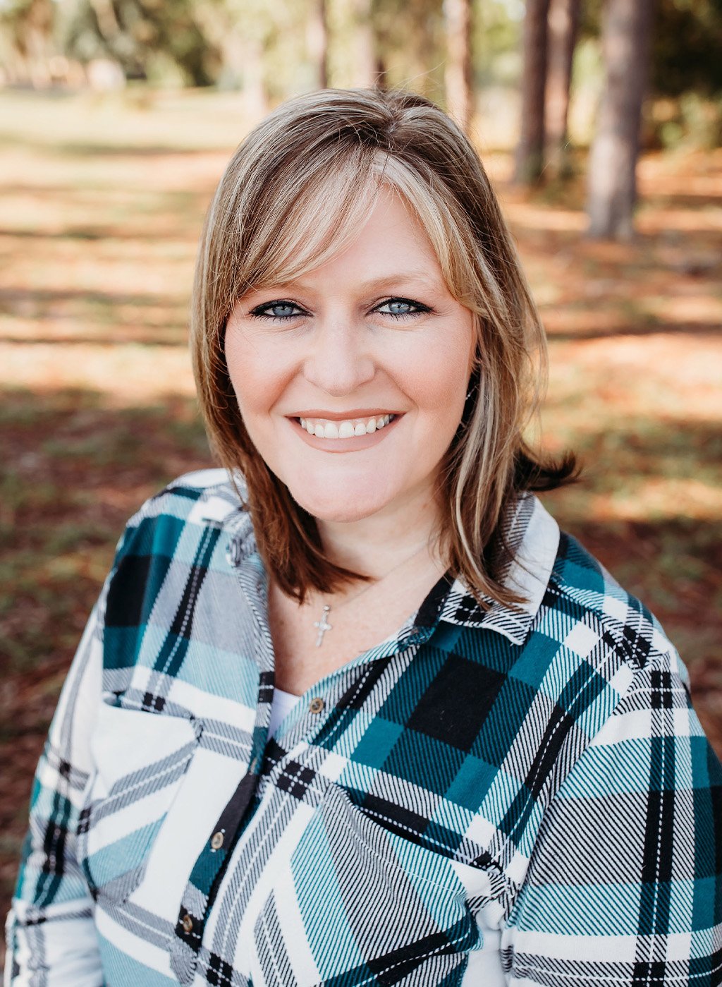 Portrait of a smiling woman with shoulder-length hair in a plaid shirt outdoors