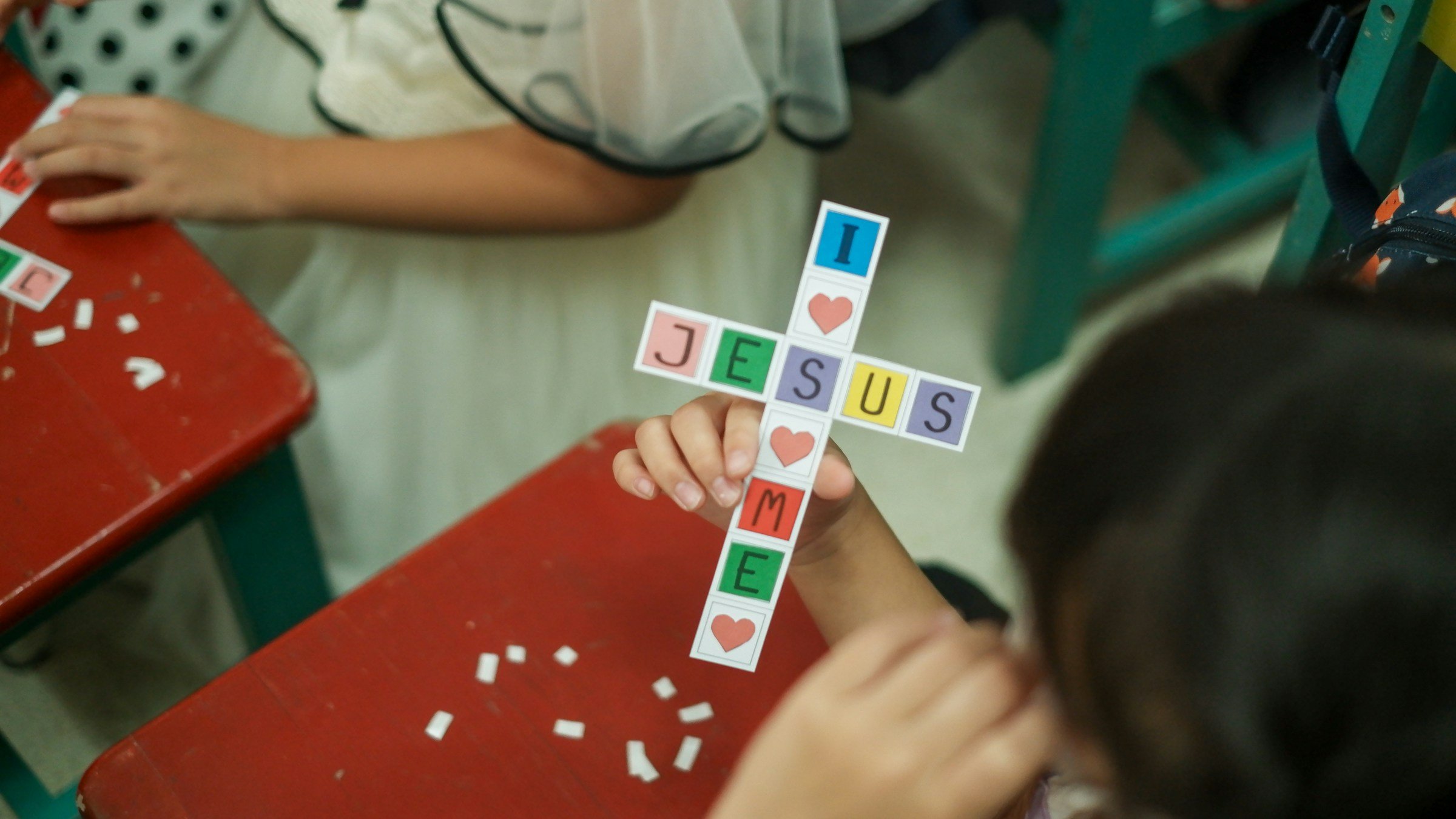 Child holding a paper cross with letters spelling JESUS