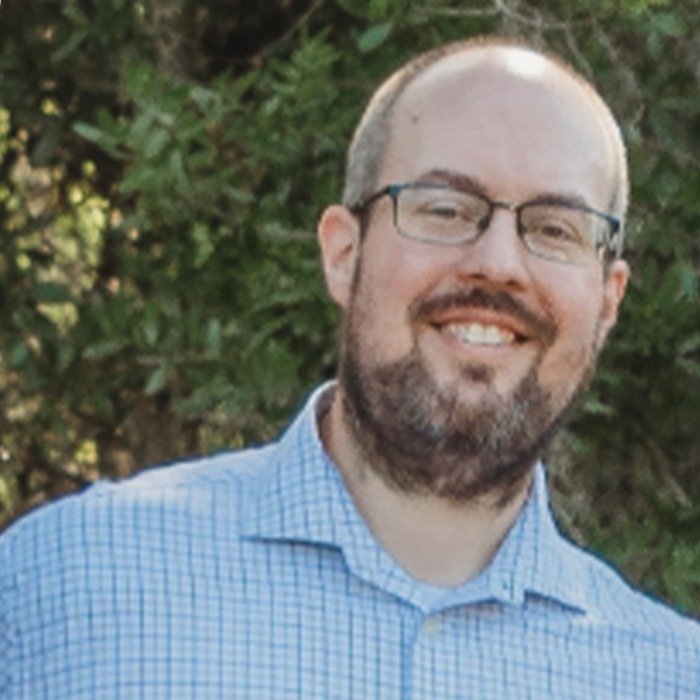 Portrait of a smiling man with glasses and a beard in a light blue shirt