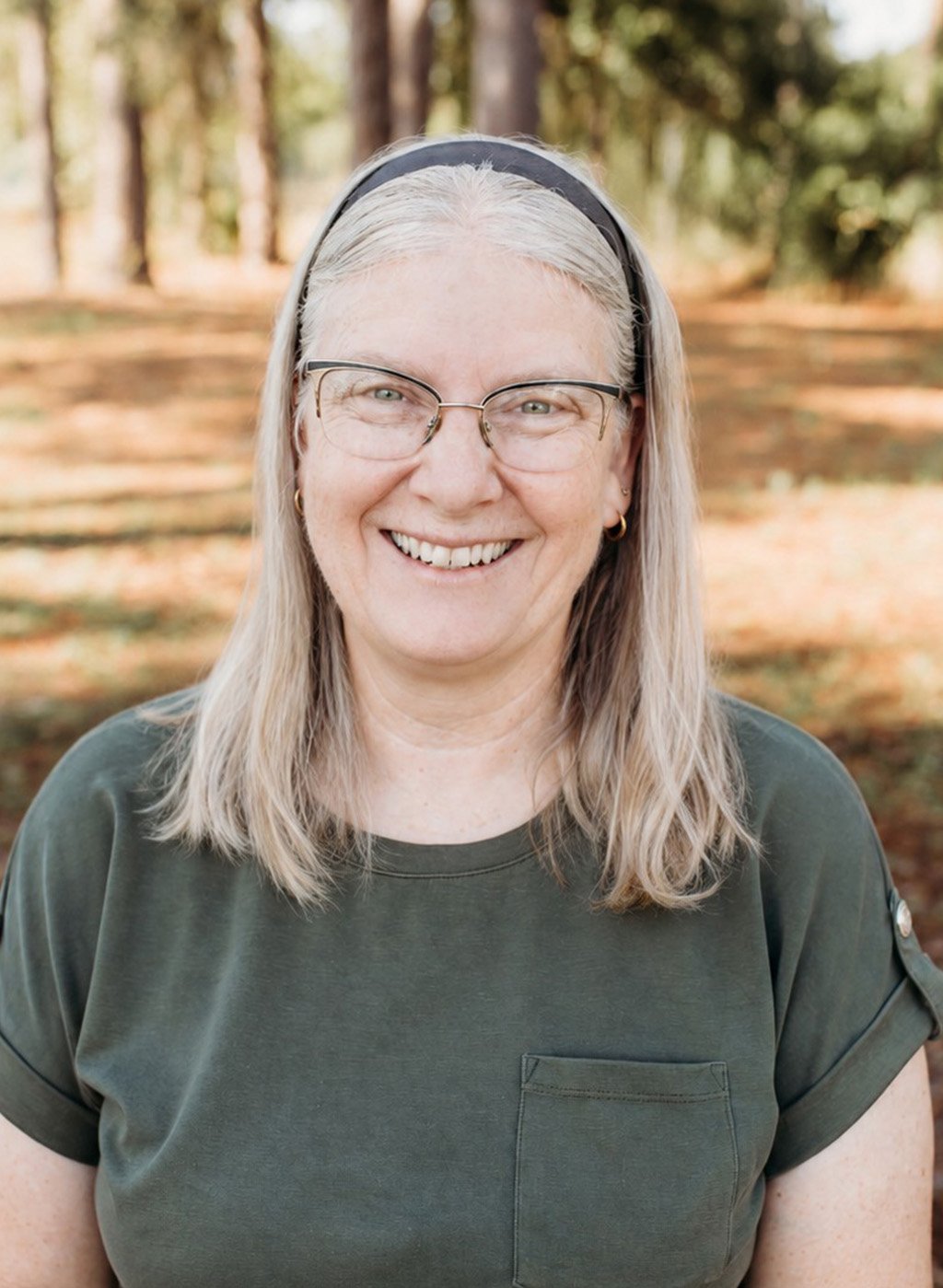 Portrait of a smiling woman with gray hair and glasses in an olive shirt outdoors