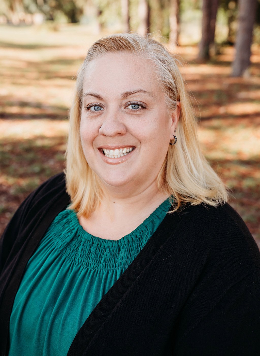 Portrait of a smiling woman with blonde hair in a teal top and black cardigan