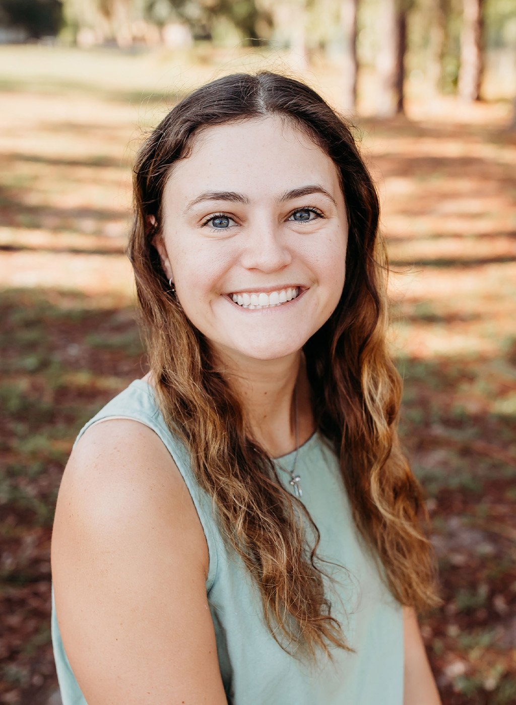 Portrait of a smiling woman with long wavy brown hair in a sleeveless top outdoors