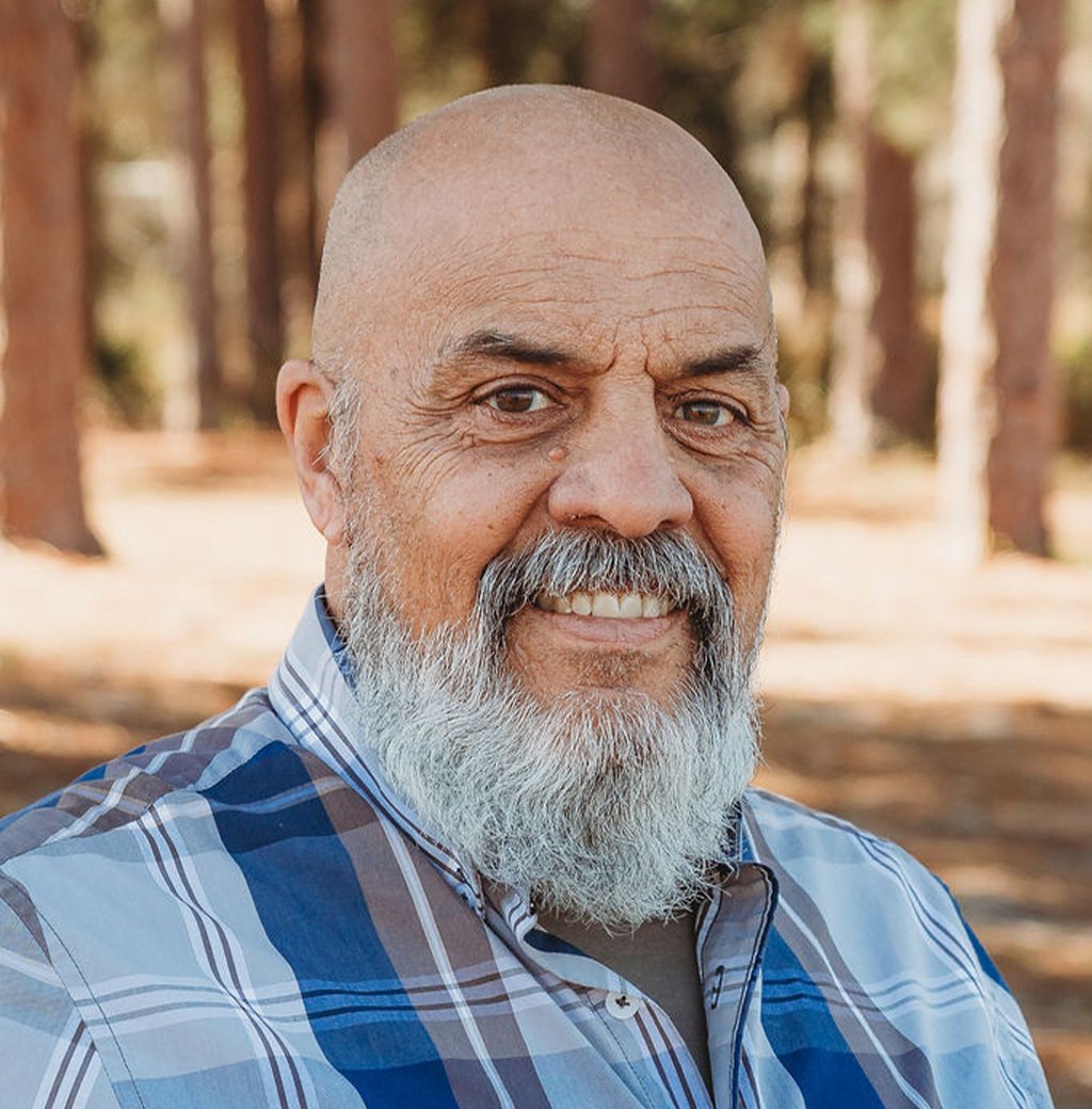 Portrait of a smiling bald man with a gray beard in a plaid shirt outdoors