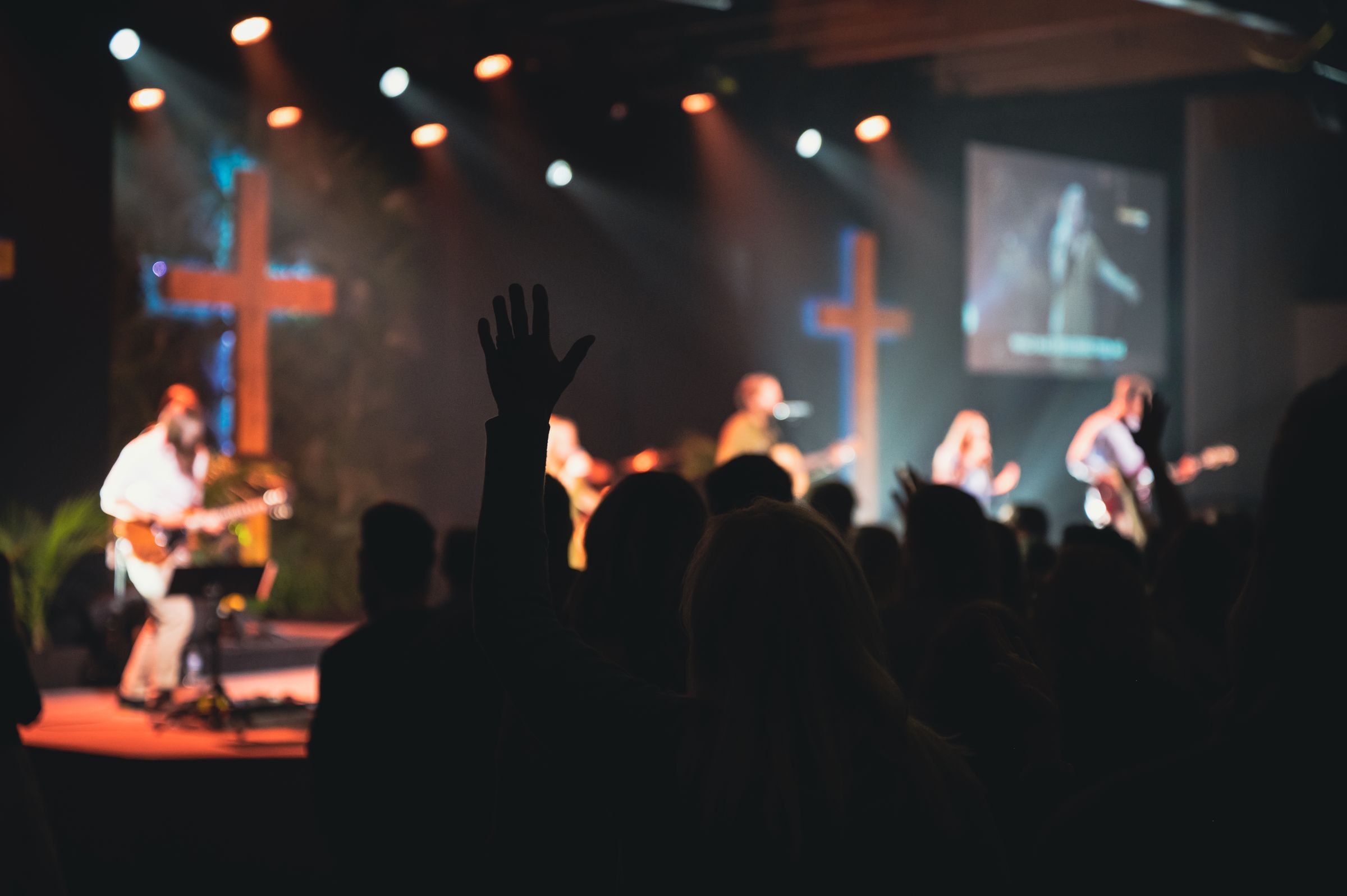 Worship band performing on a dimly lit stage with two crosses while the audience raises hands