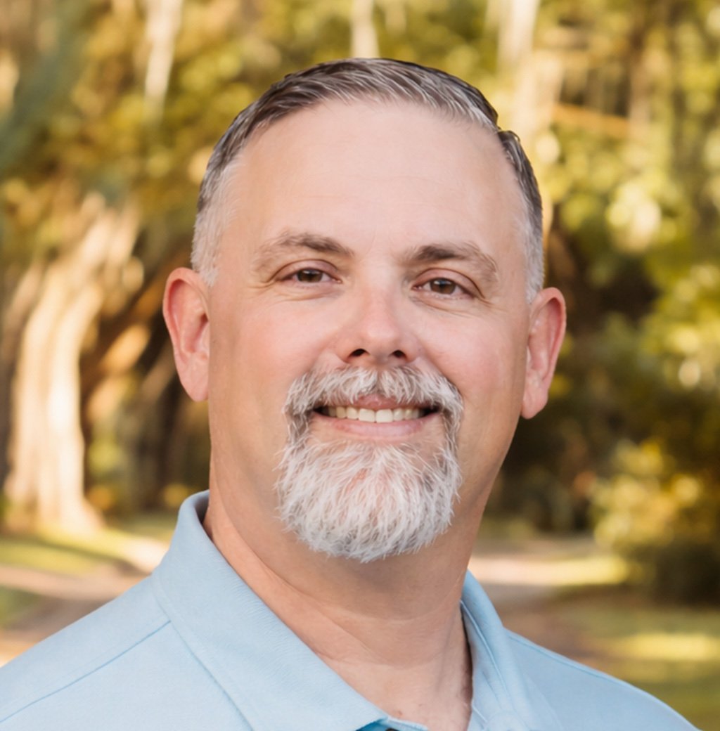 Portrait of a smiling man with gray hair and a gray beard in a light blue shirt