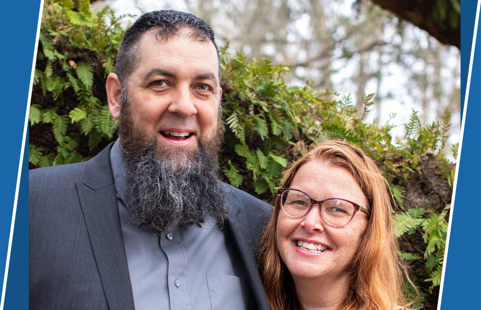 Smiling bearded man in a blazer beside a smiling woman with glasses, outdoors