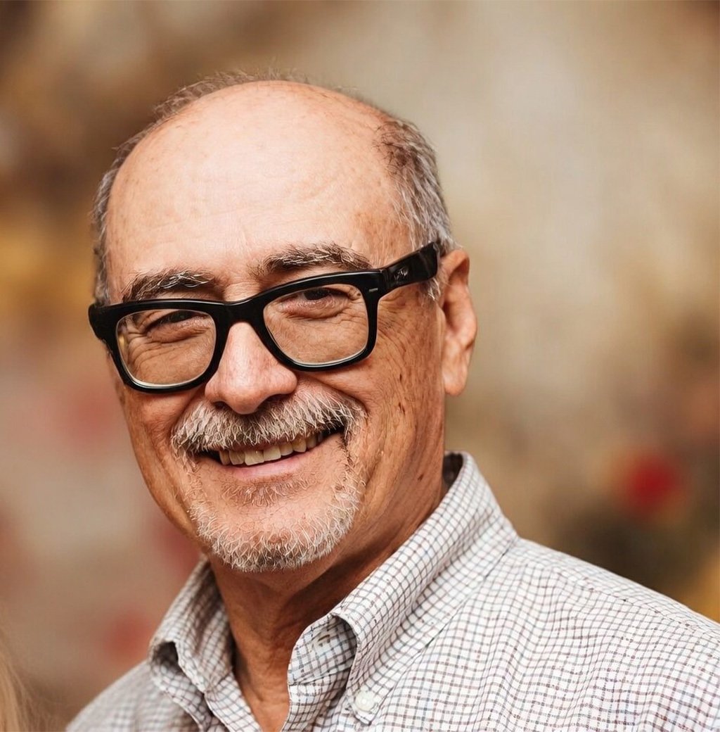 Portrait of a smiling older man with dark-framed glasses and a mustache