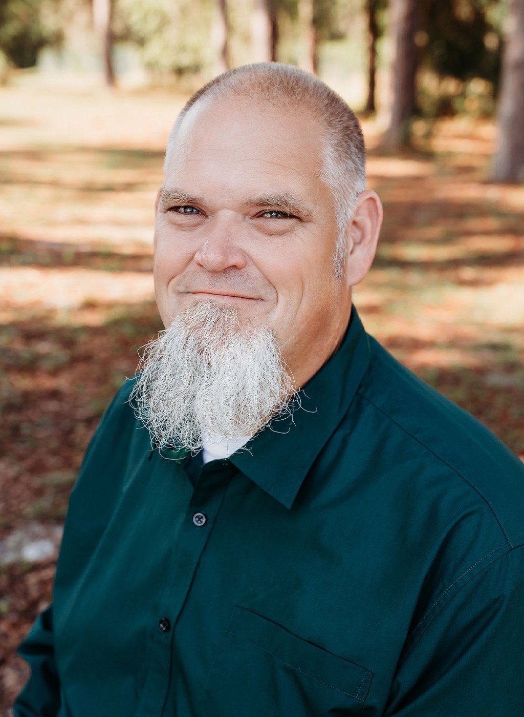 Portrait of a smiling man with a gray goatee in a dark green shirt outdoors