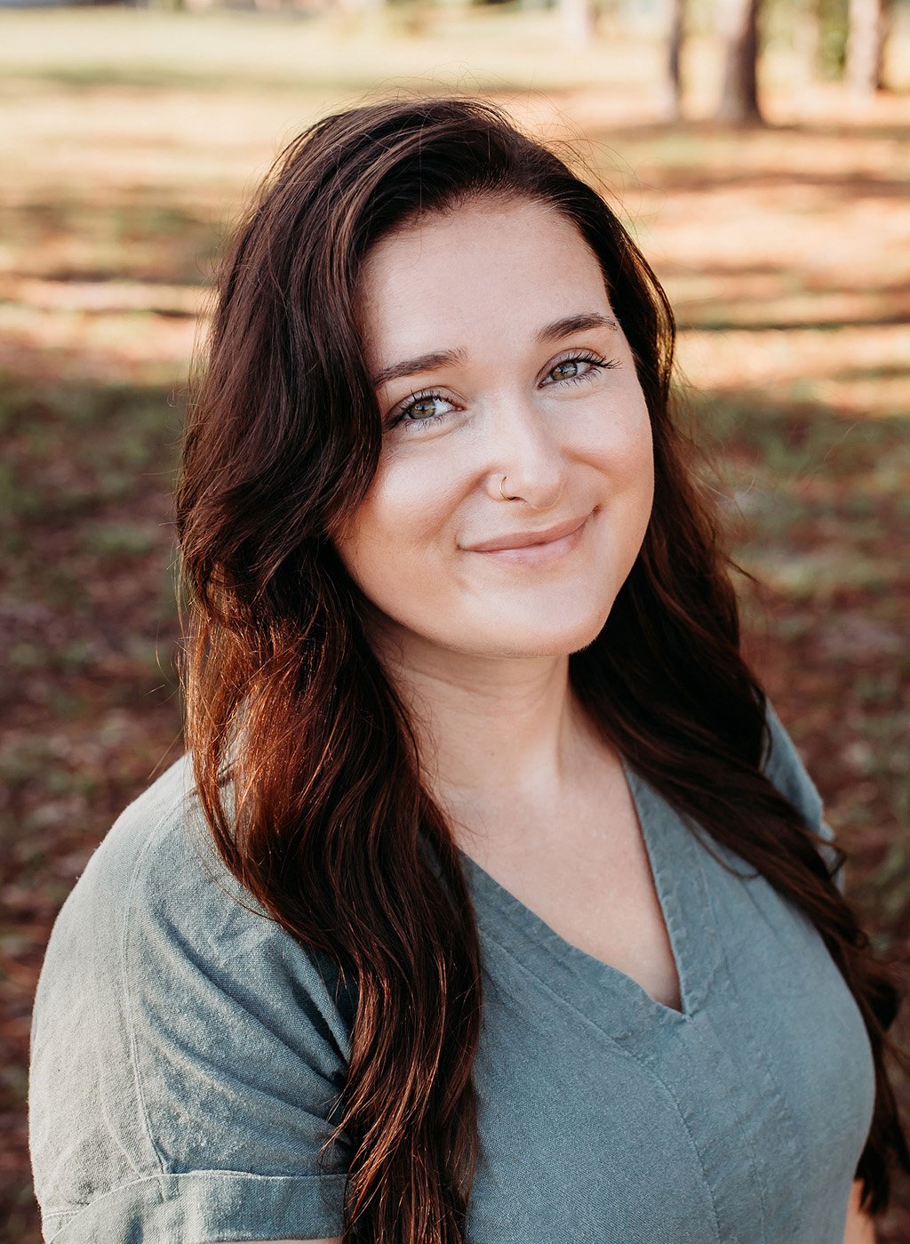 Portrait of a smiling woman with long dark hair in a gray top outdoors